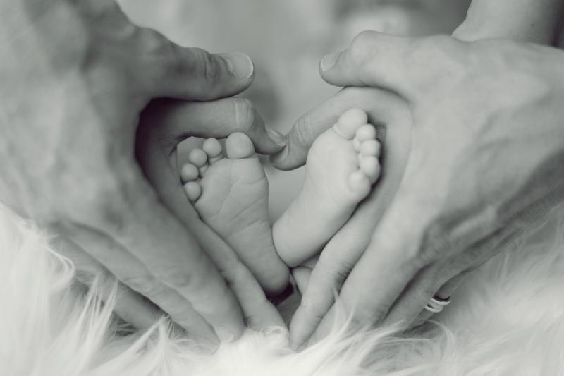 Black and white photo of parents' hands forming heart shape around newborn feet